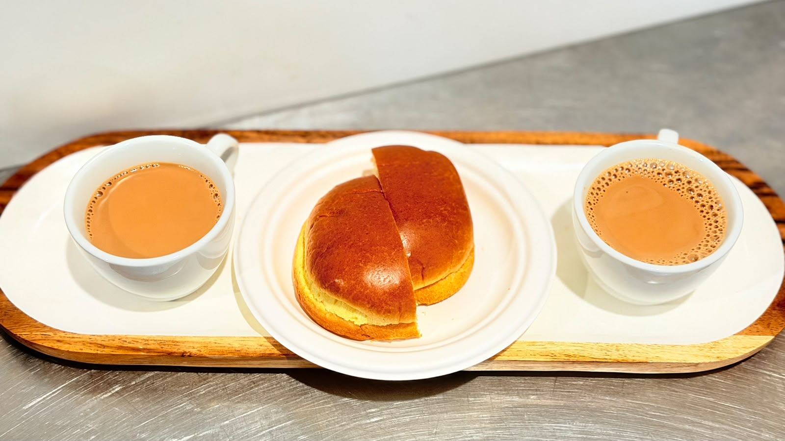 Two cups of signature Kadak Chai served with a fresh butter bun on a wooden tray at Tandoor and Chai Bedford Perth